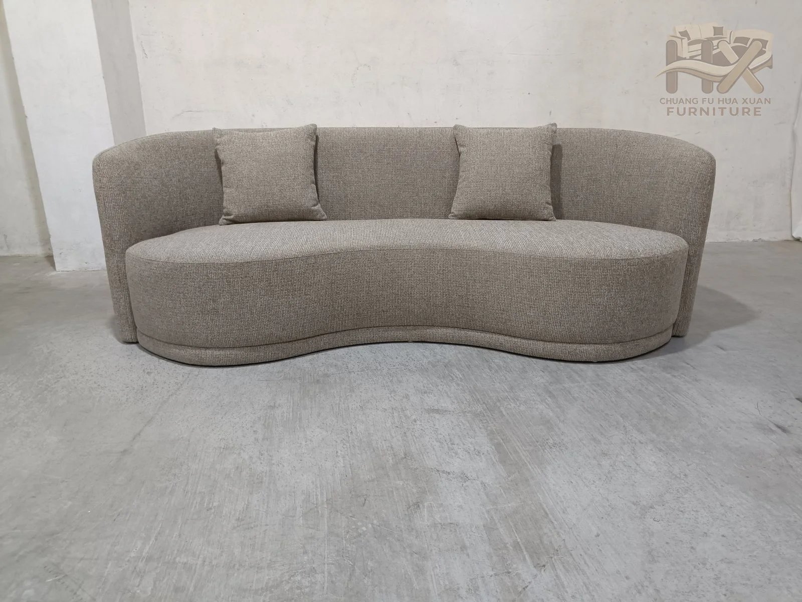 A broad back and rounded ends form a continuous soft curve, with loose back cushions sitting inside the low upholstered shell.