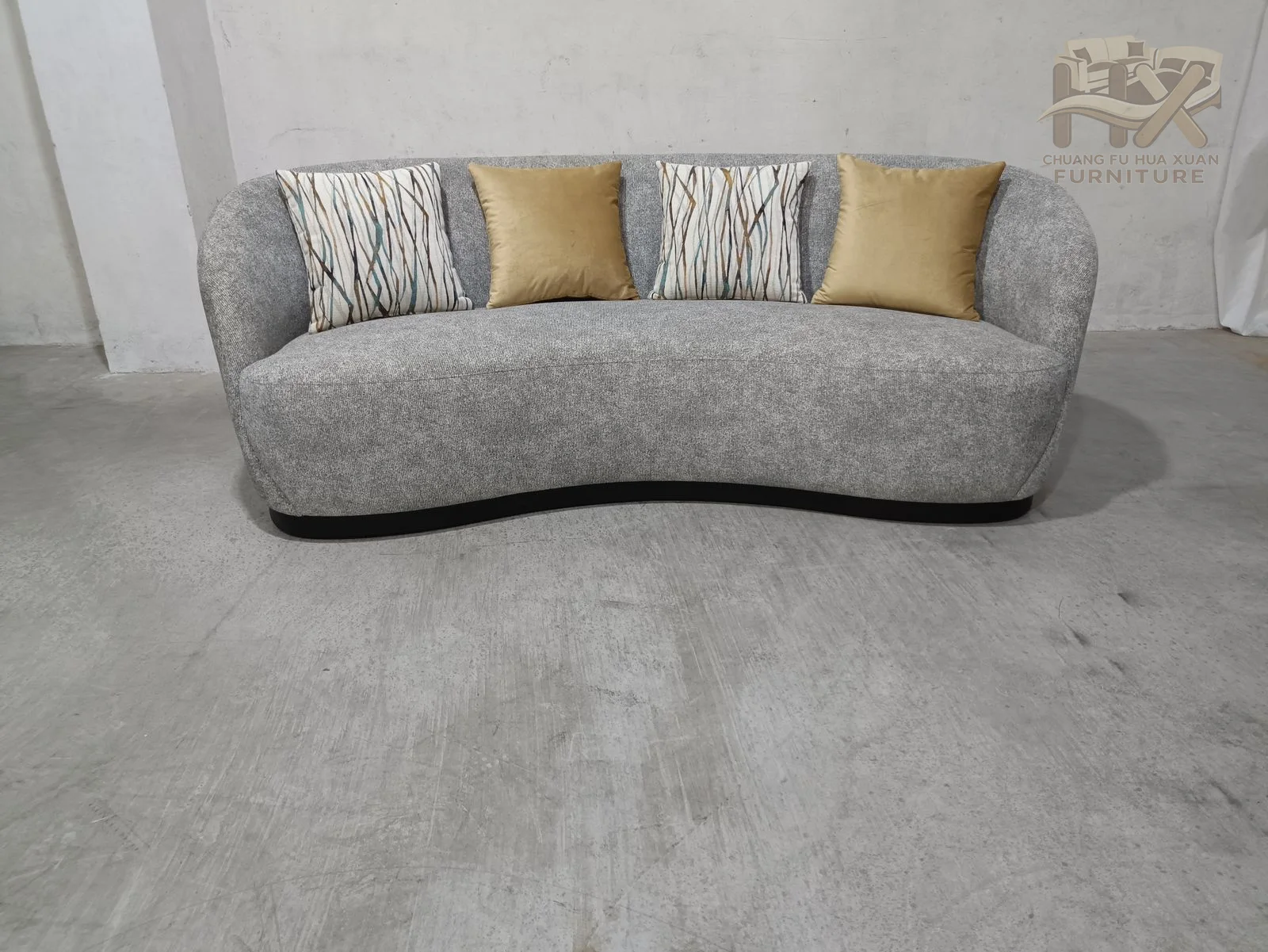 The front edge bends in a shallow wave while the back wraps around the ends, carrying patterned accent cushions within the grey shell.