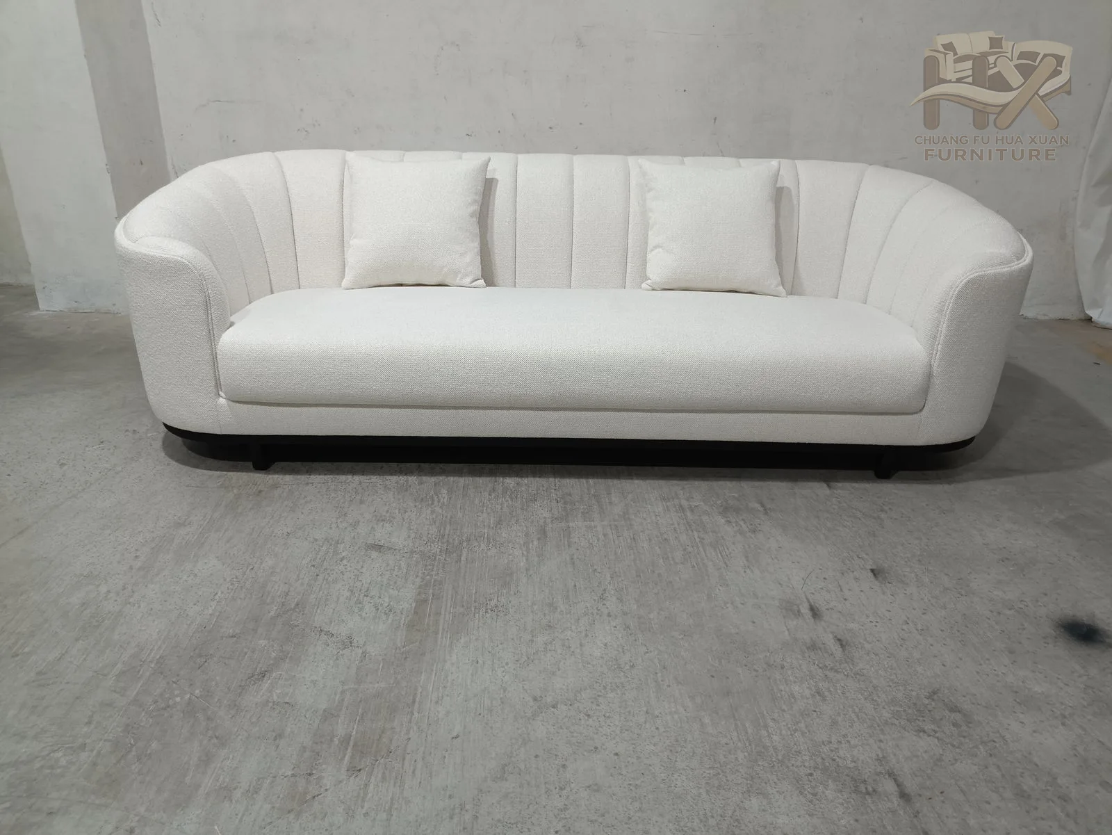Wide vertical channels run over the rounded backs and arms of the white sofa and companion chair, with a low dark plinth below.