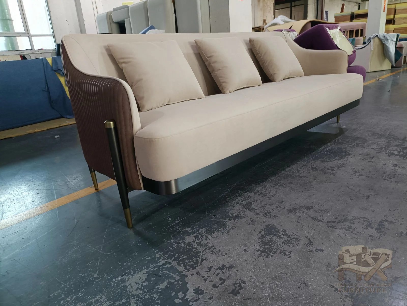 The sofa pairs pale seat and back cushions with darker brown outer arms and a slim exposed base.