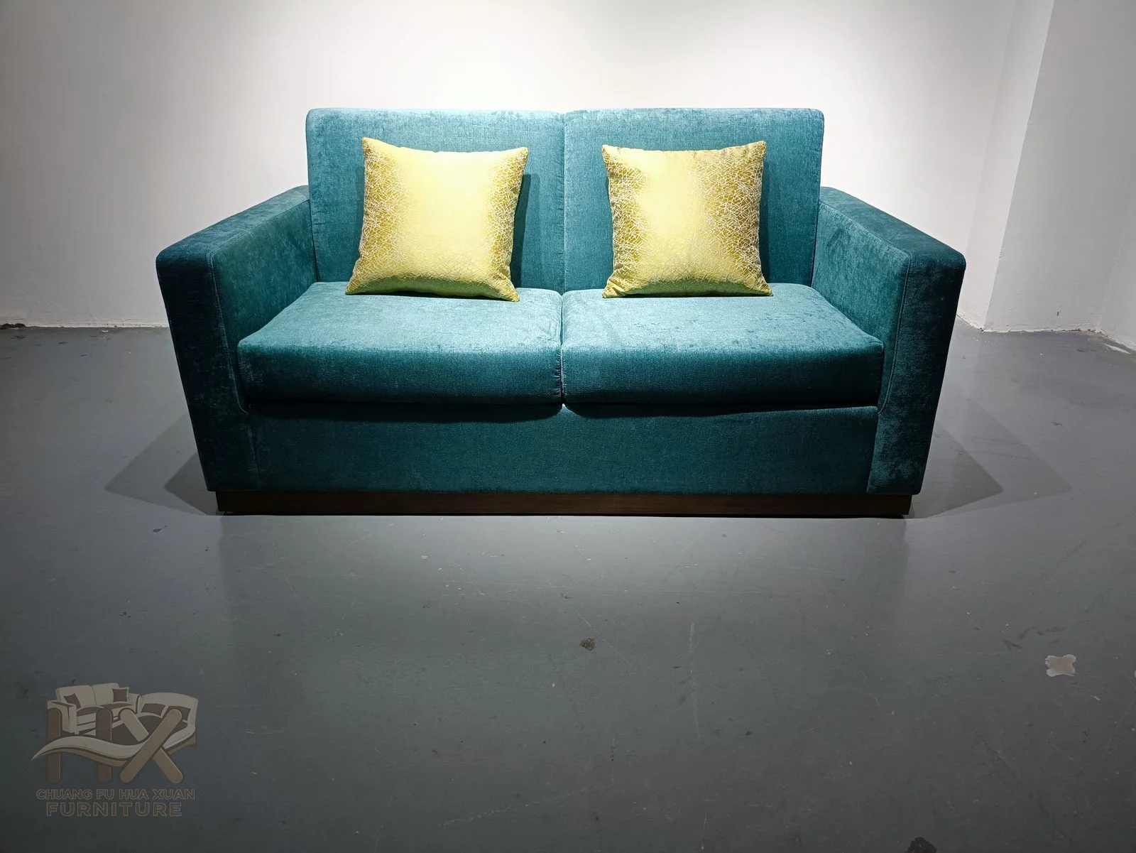 A low teal two-seat sofa combines straight upholstered arms with small contrasting loose cushions.