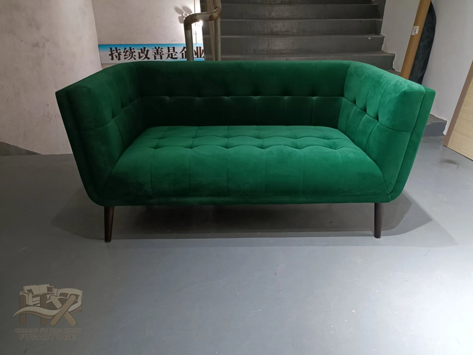 Buttons mark the inner back of an emerald sofa whose ends curve forward around a straight cushioned seat.