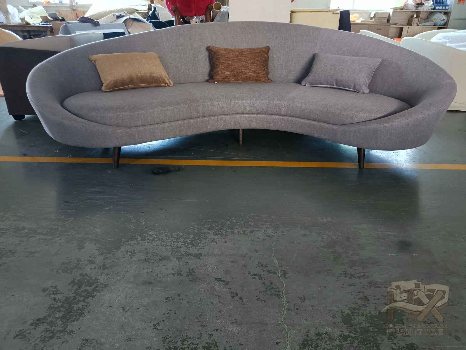 Pale silver upholstery follows a long arc above a narrow raised base, with loose pillows spaced along the back.