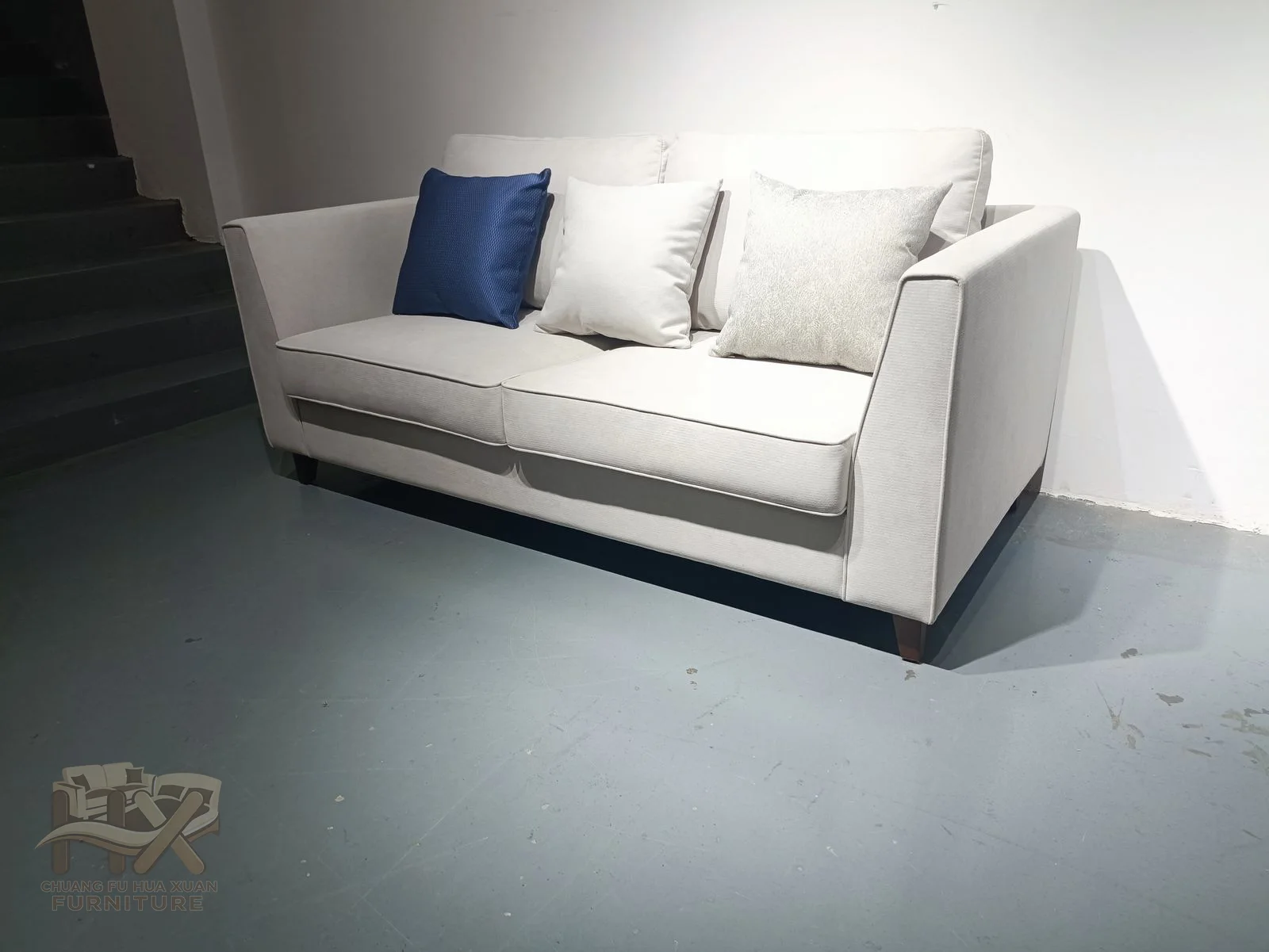 Square white arms and pale loose cushions repeat across several seating widths, with blue accent pillows punctuating the back.