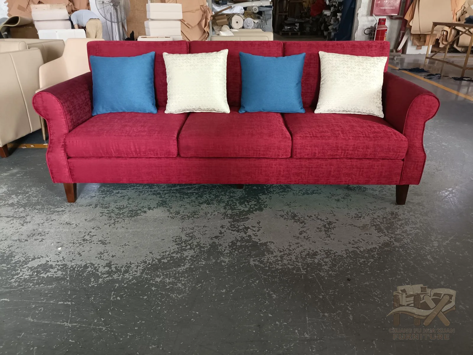 Bright red upholstery covers the full sofa frame, while alternating blue and white pillows line its low back.