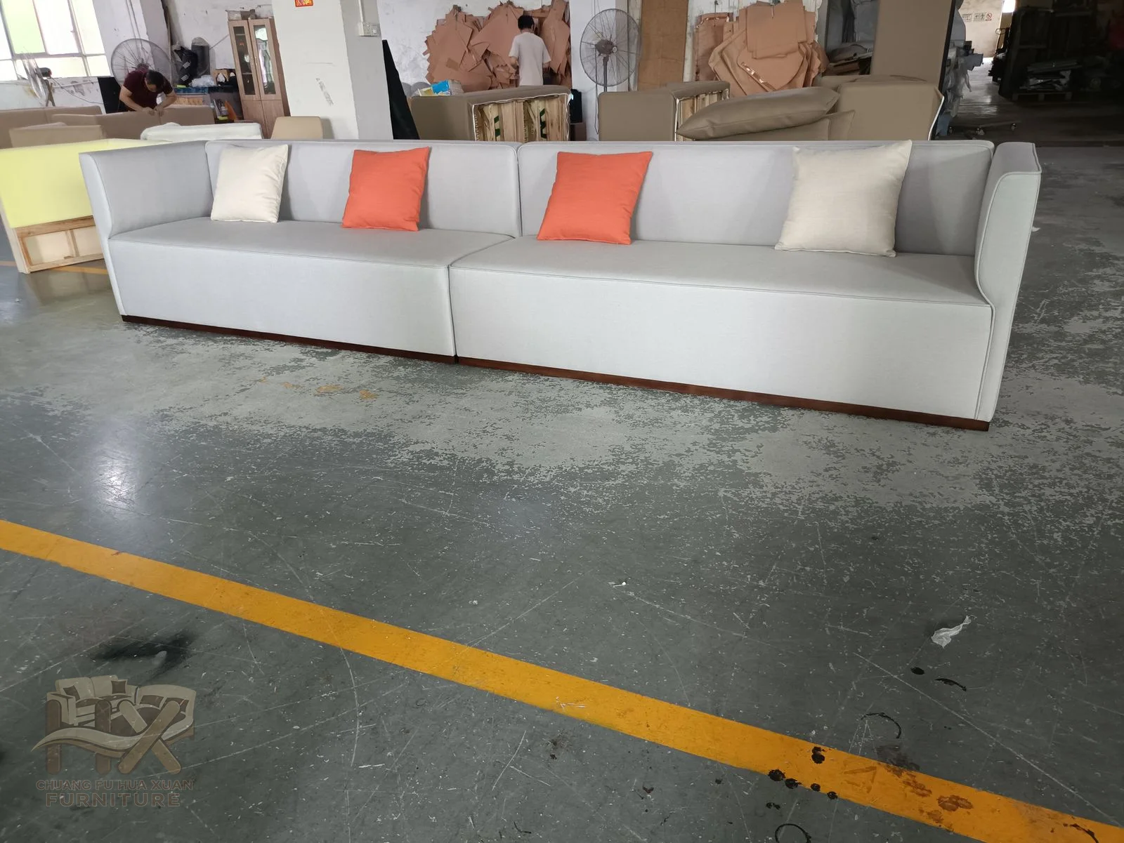 A long white seat and straight arms carry a row of small warm-coloured back cushions.