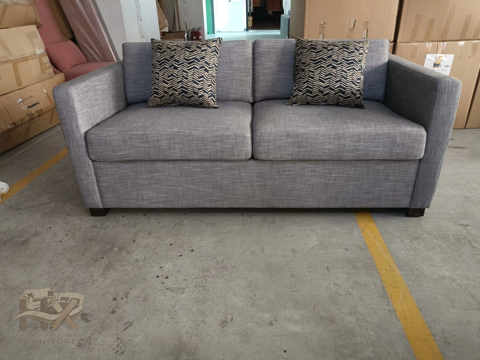 A compact grey sofa carries patterned loose pillows above a low straight back and square arms.