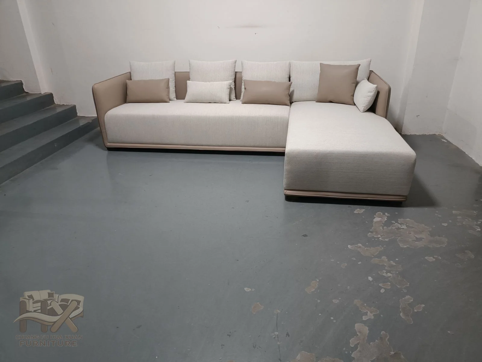 A pale sofa turns into a chaise extension with low straight arms and a repeated row of loose cushions.