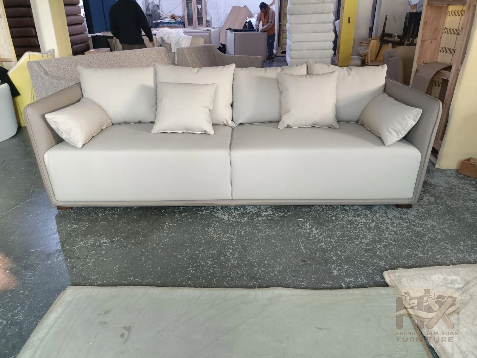 Pale loose cushions fill a low sofa with softly rounded narrow arms, shown across nearby seating widths.