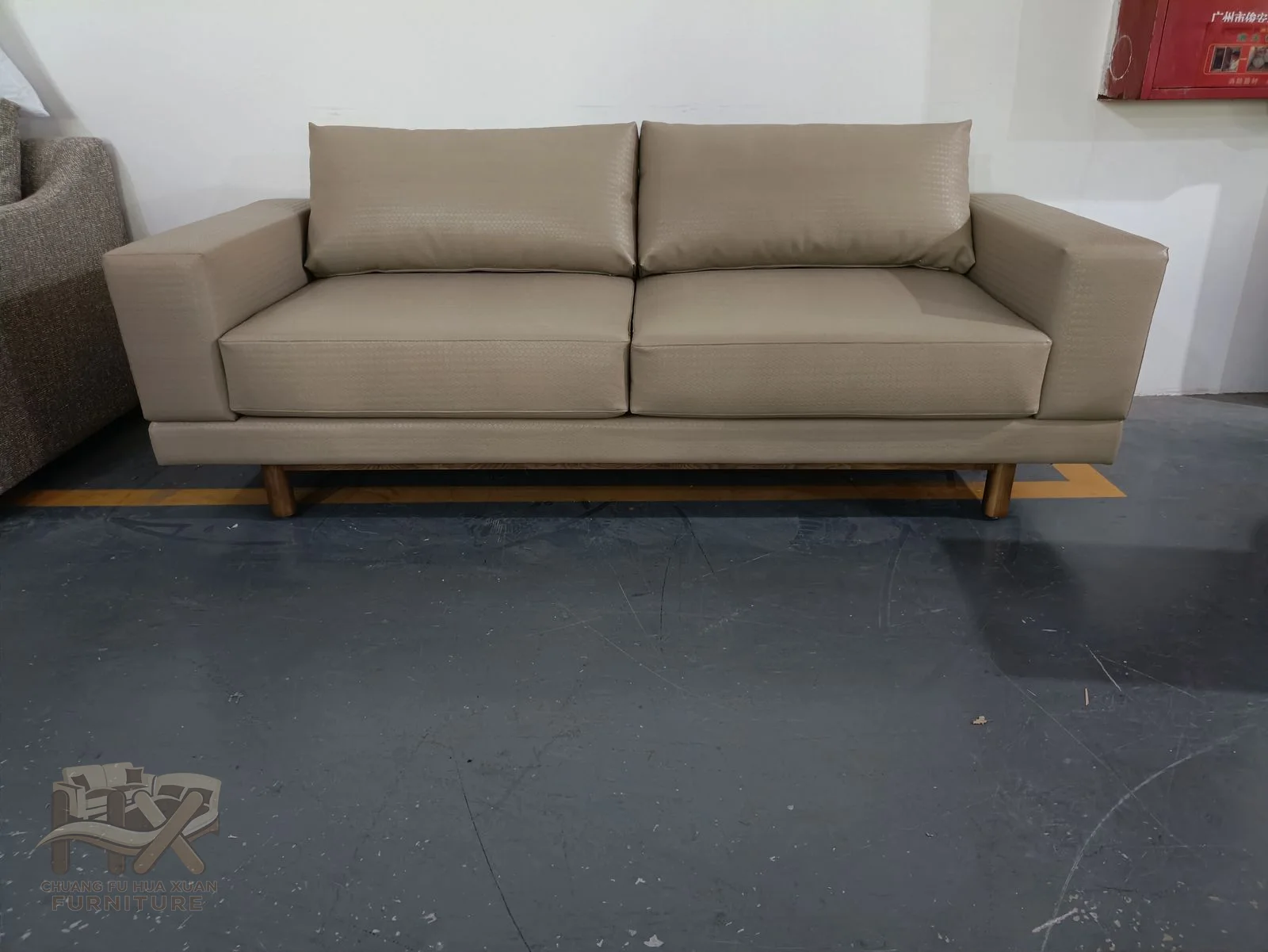 A pale sofa carries loose cushions between straight padded arms above a slim exposed foot line.