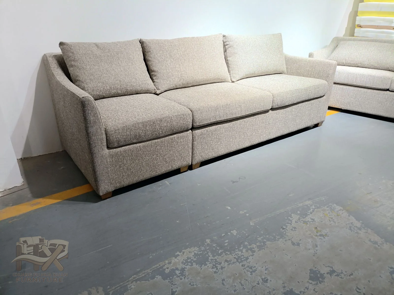 A pale three-seat sofa uses low cushioned arms and a straight loose back, shown in closely related upholstery tones.