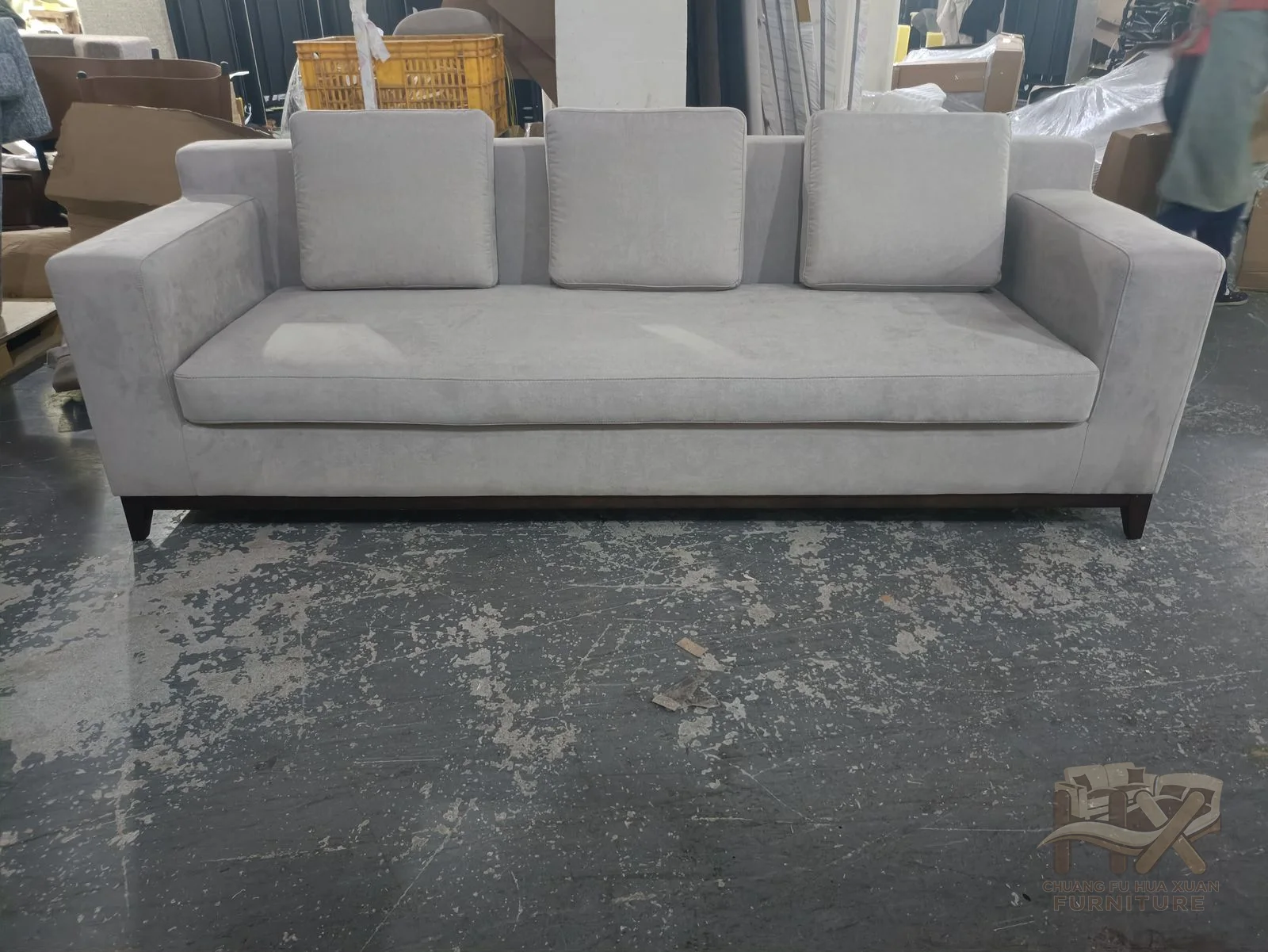A grey sofa pairs a low arm line with generous loose cushions and a shallow raised base.