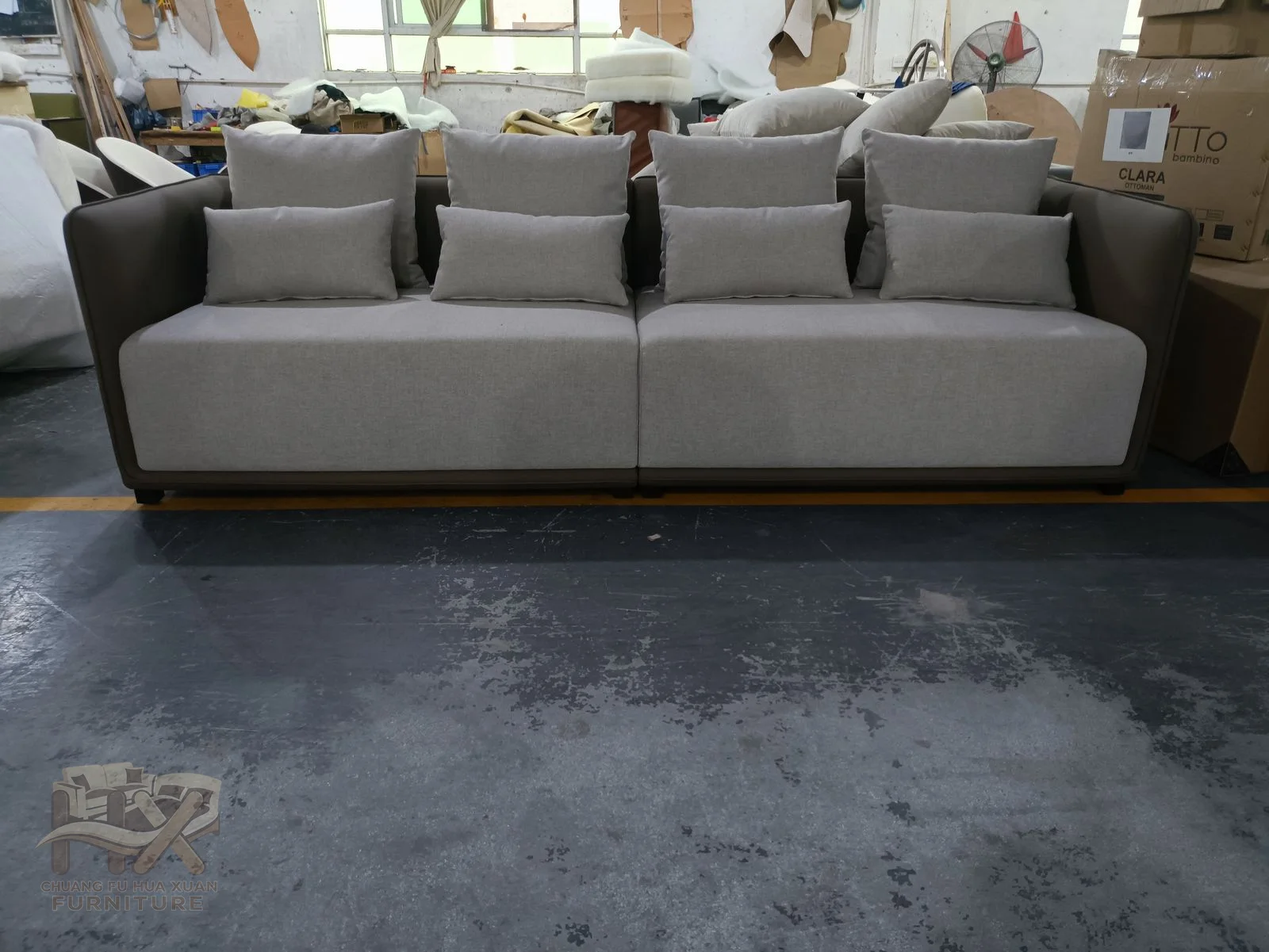 A grey three-seat sofa uses softly padded arms and loose back cushions above a low base.