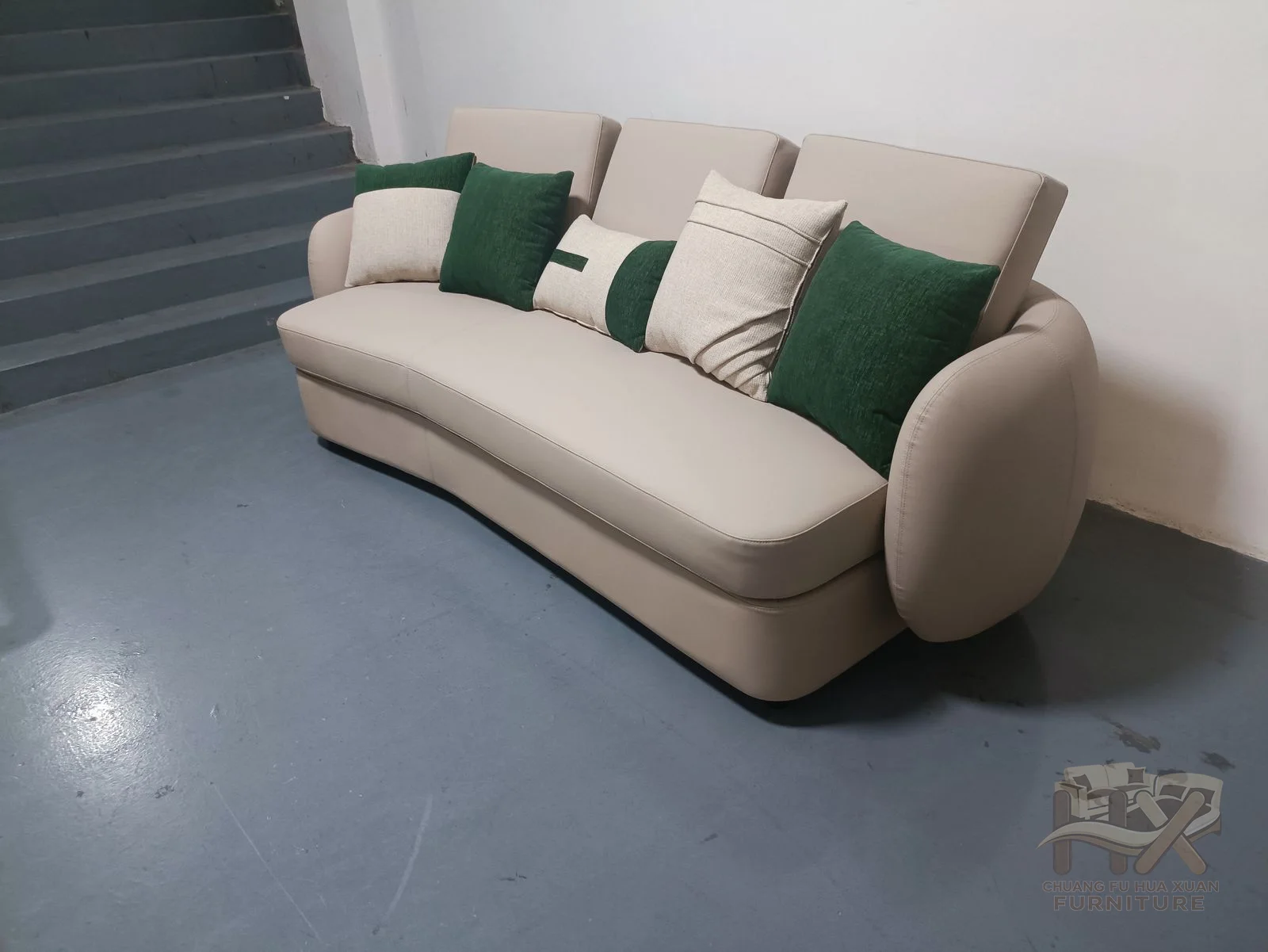 A pale sofa bends around a low continuous back with a small green upholstered accent section.