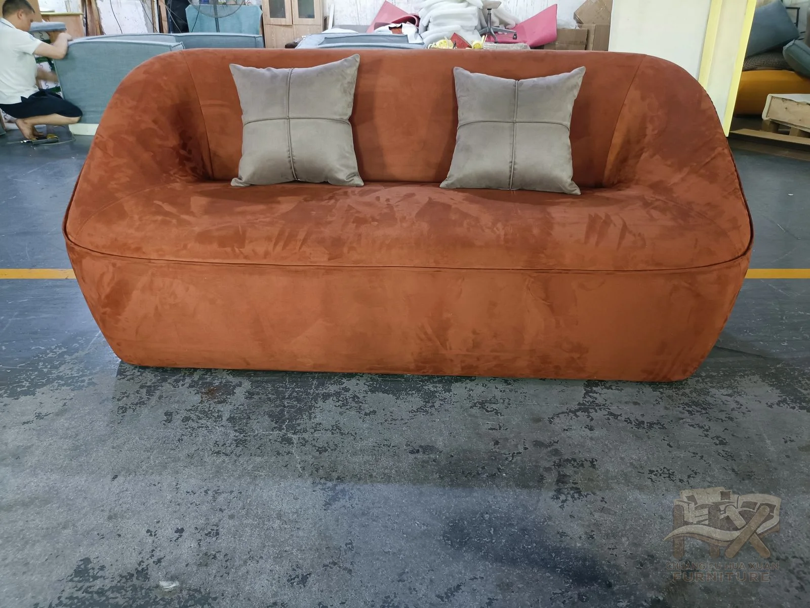 A rust-coloured sofa has gently curved arms and a deep continuous cushioned seat.