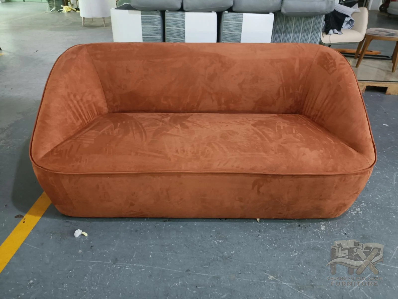 A small rust sofa rounds its back into short arms around a single broad seat.