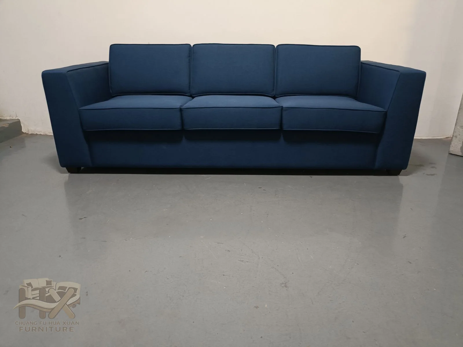 A deep blue sofa carries two broad seat cushions between straight substantial upholstered arms.