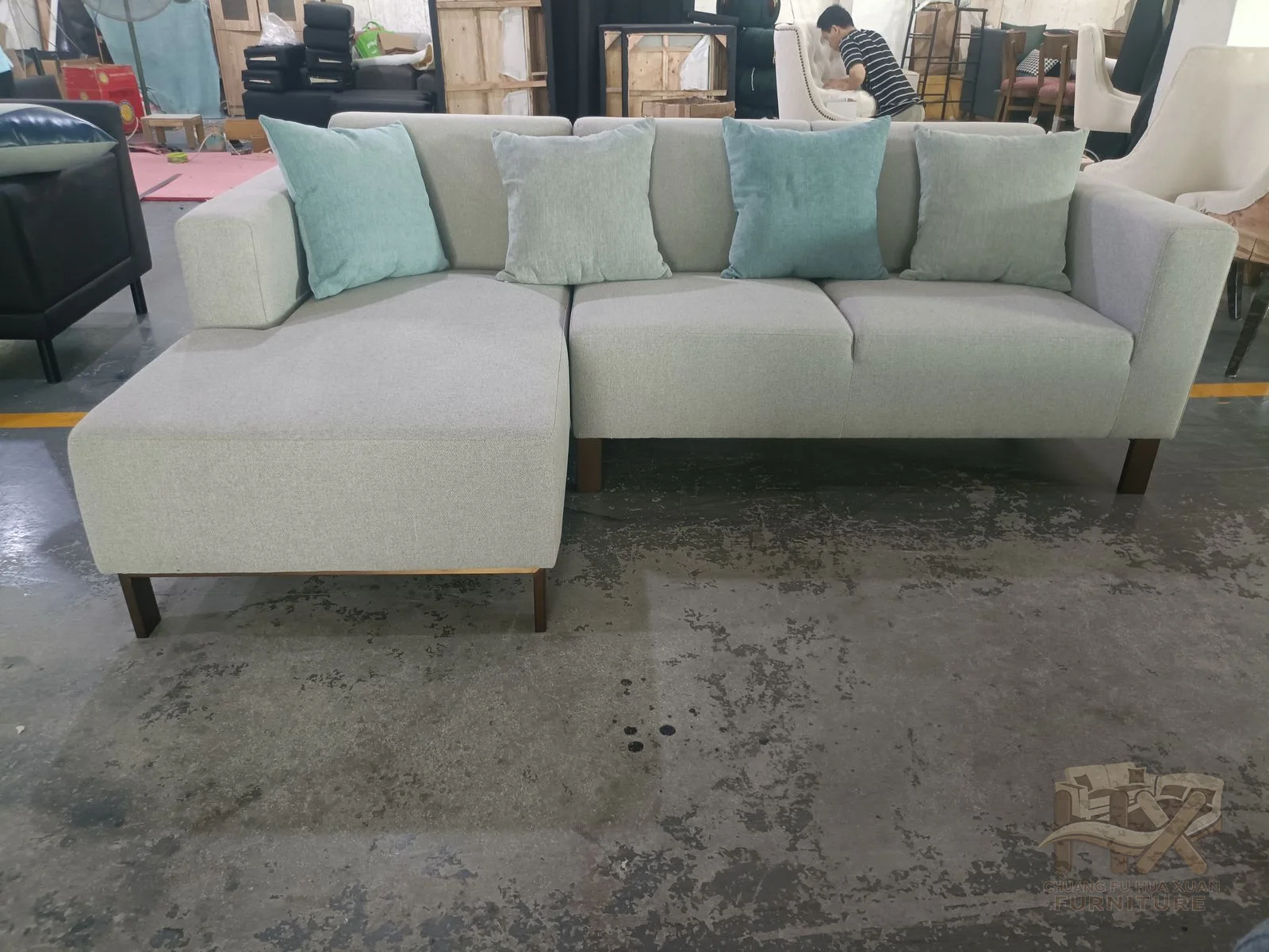 A pale corner sofa uses low square arms and matching broad ottoman beside its cushion run.