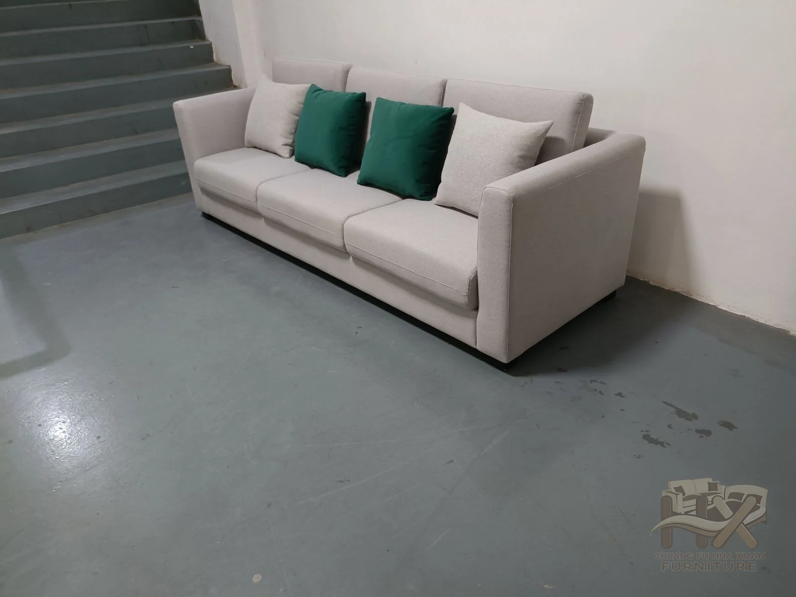 An ivory sofa has slim padded arms and a straight seat run highlighted by dark green cushions.