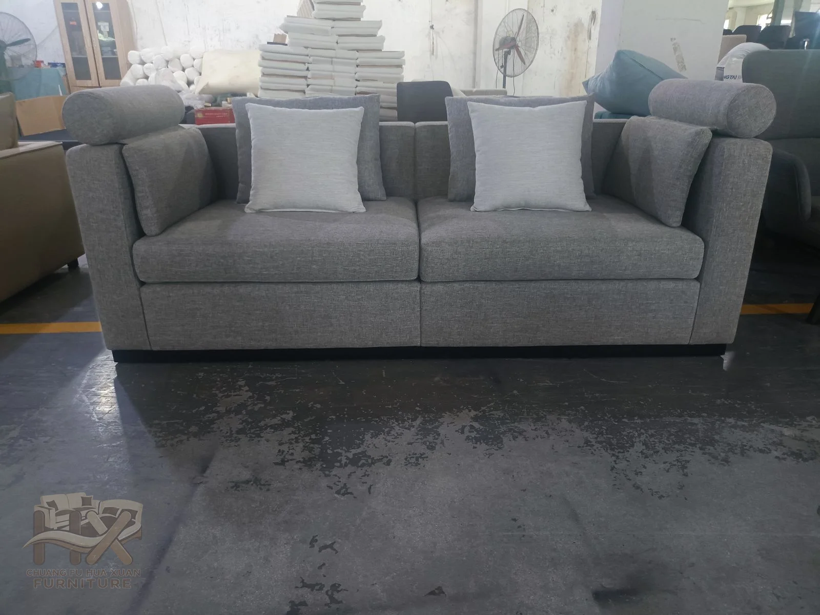 A grey sofa carries three deep seats and generous loose backs between broad arms.