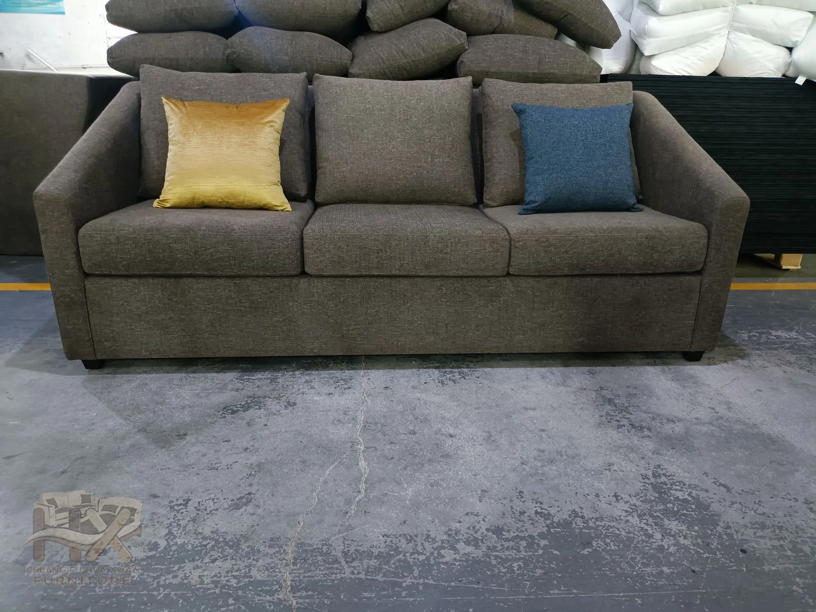 A charcoal sofa uses straight low arms and loose yellow and blue accent cushions.
