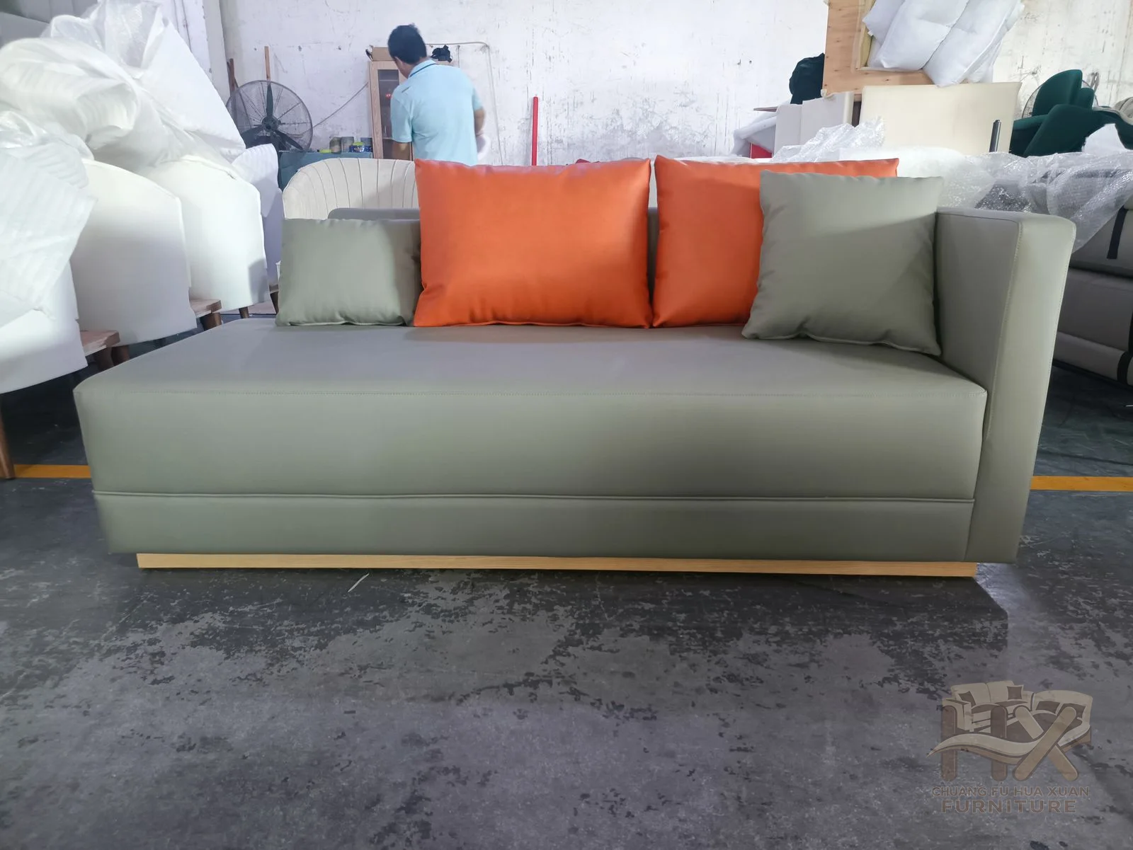 A pale straight sofa carries orange loose cushions between short square arms.