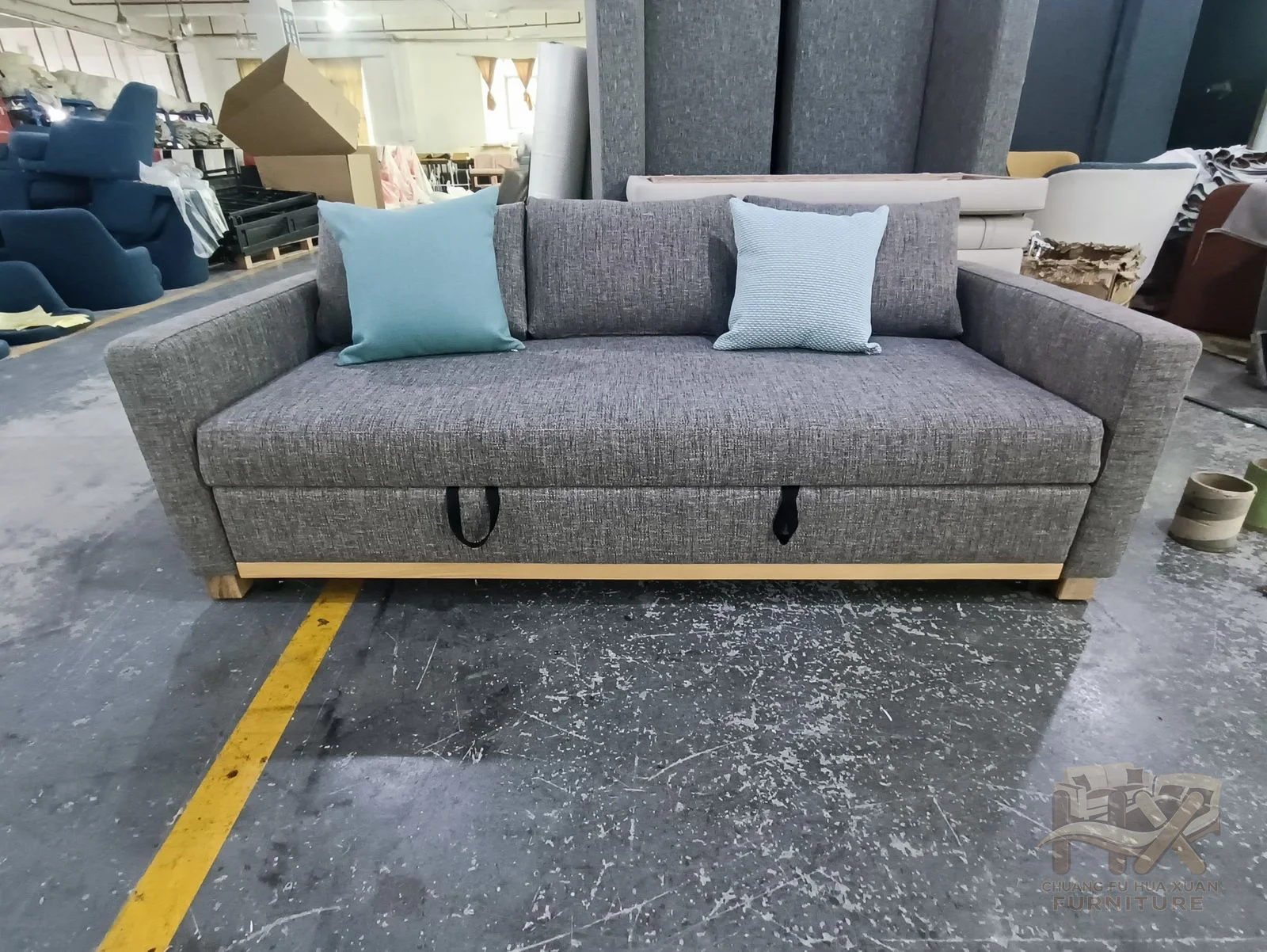A grey sofa supports loose blue and pale back cushions above a narrow exposed metal-look base.