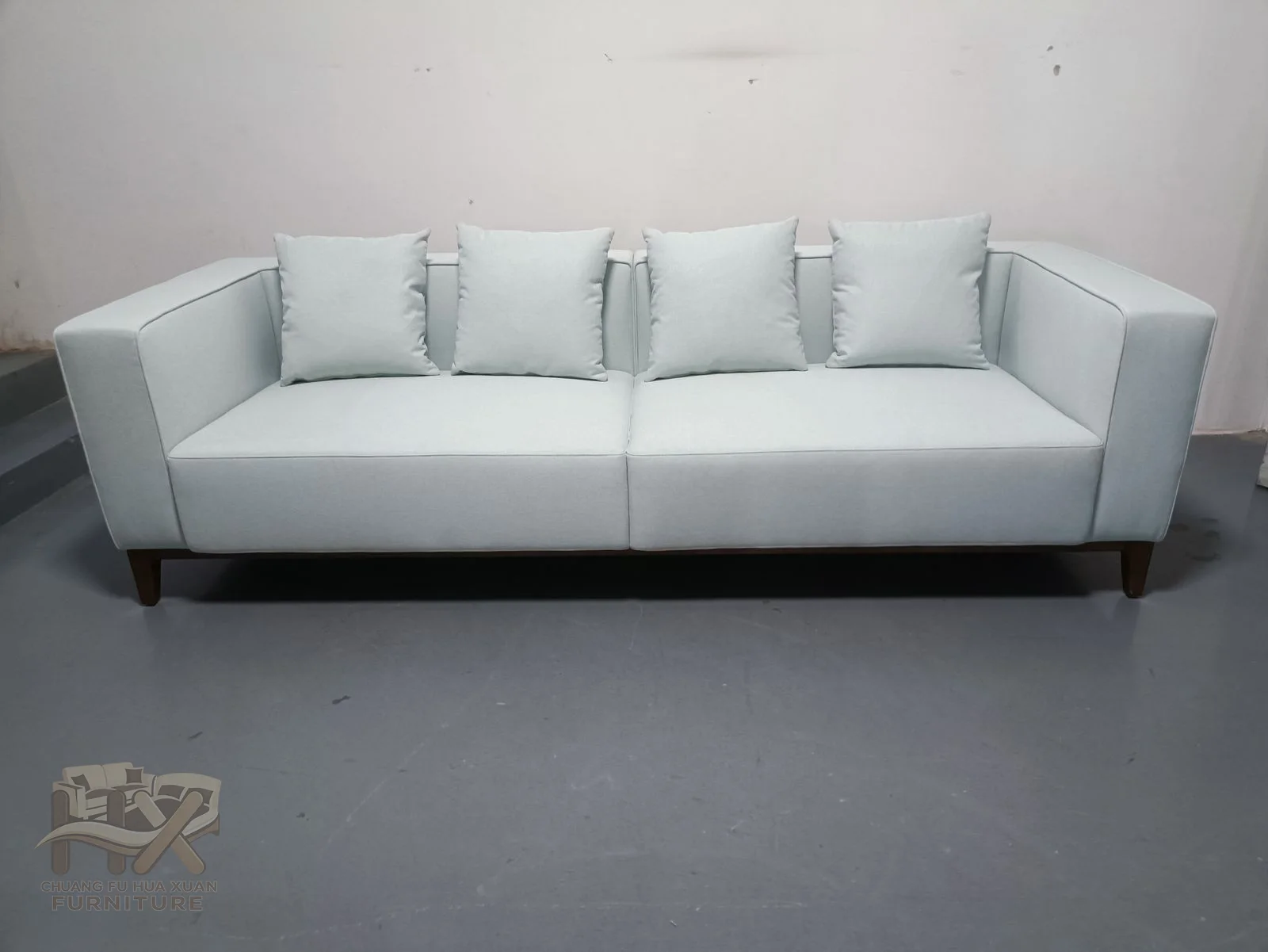 A long white sofa repeats broad back cushions between low straight padded arms.