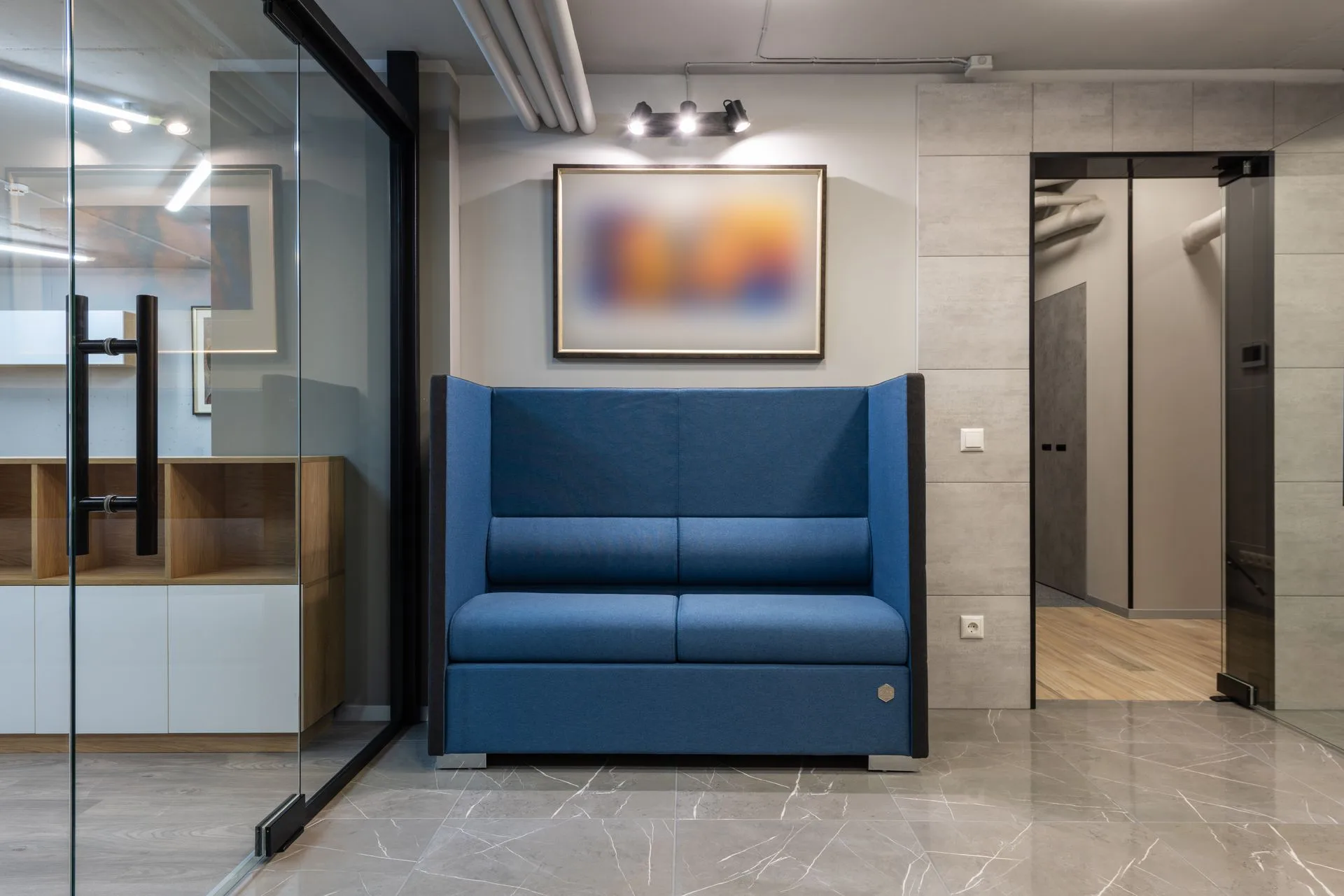 Blue upholstered sofa beside glass meeting-room partitions in a contemporary office reception